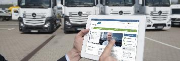 
Speditér stojí před svým nákladním automobilem a drží v ruce tablet, na displeji je zobrazen zákaznický portál společnosti Toll Collect.